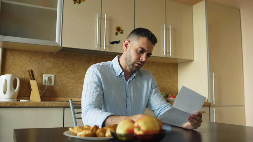Un homme lit attentivement un courrier à la table de sa cuisine.