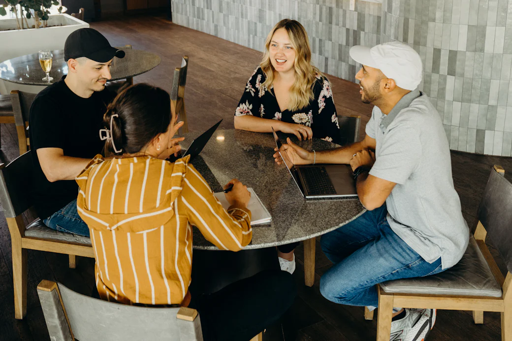 Quatre collègues échangent autour d’une table ronde, ordinateurs ouverts.